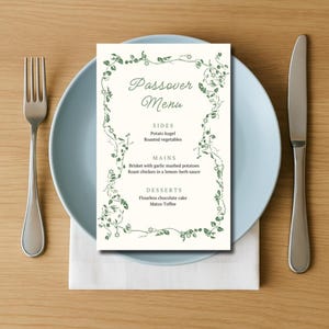 May include: A white card with a green floral border and the text "Passover Menu" printed in black. The menu lists the following items: Sides: Potato kugel, Roasted vegetables; Mains: Brisket with garlic mashed potatoes, Roast chicken in a lemon-herb sauce; Desserts: Flourless chocolate cake, Matzo Toffee.