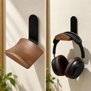 May include: A wall-mounted headphone stand featuring a curved, natural-toned wooden support attached to a vertical black metal bracket. The bracket is secured with a single visible screw, providing a sturdy base for resting over-ear headphones.