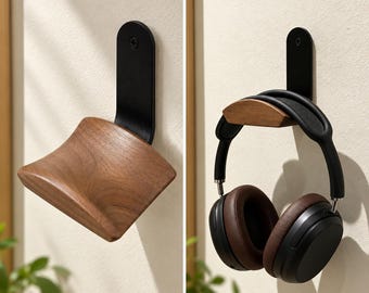 May include: A wall-mounted headphone stand featuring a curved, natural-toned wooden support attached to a vertical black metal bracket. The bracket is secured with a single visible screw, providing a sturdy base for resting over-ear headphones.