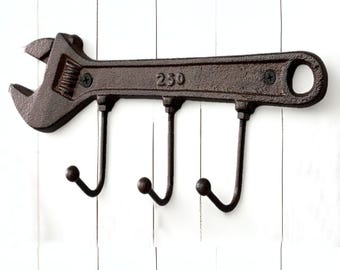 May include: A rustic, brown cast iron wrench-shaped wall hook with three curved hooks. The wrench has the number "230" embossed on it. The wall hook is mounted on a white wooden surface.