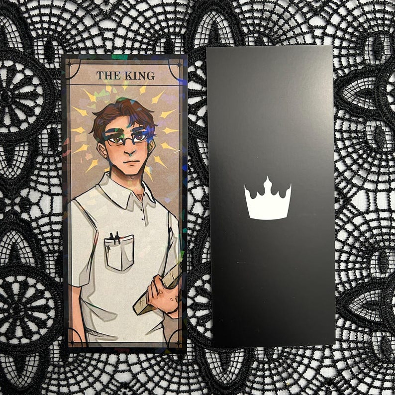 Op de afbeelding: Een tarotkaart met de tekst "THE KING" en een illustratie van een persoon met een bril en een wit overhemd, die een boek vasthoudt. Daarnaast een zwarte kaart met een witte kroon.