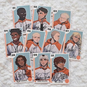 Op de afbeelding: Een verzameling van tien verzamelkaarten met illustraties van mensen in oranje en witte sportkleding. Elke kaart heeft een uniek portret, een nummer en een handtekening. De kaarten liggen op een wit, gestructureerd oppervlak.