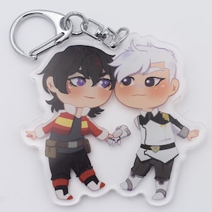 May include: A clear acrylic keychain featuring two cartoon characters holding hands. One character has black hair and wears a red jacket, the other has white hair and wears a white uniform. The keychain has a silver clasp.