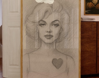 May include: A framed pencil sketch portrait of a person with wavy hair and a heart shape on their chest. The artwork is displayed in a light wood frame, positioned in a room with wooden floors and other framed prints on the wall behind it.