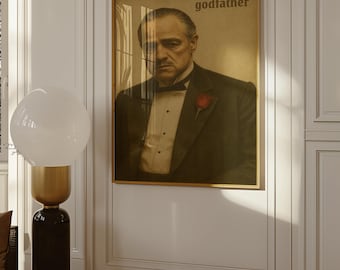 Op de afbeelding: Een ingelijste rechthoekige wandposter met een sepia-kleurig portret van een man in een smoking met een rode roos op de revers en een vlinderdas. De tekst "godfather" staat in de rechterbovenhoek van de poster, die in een gouden lijst zit.