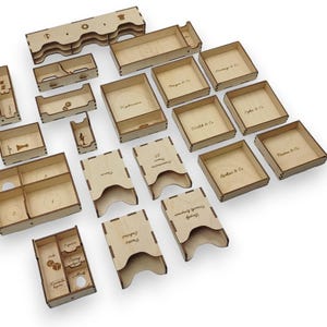 May include: A collection of laser-cut wooden game organizer components. Various shapes and sizes include trays, boxes, and dividers. Some pieces have engraved text, such as "Phantasms & Co." and "Scythe & Co.", suggesting a board game theme.