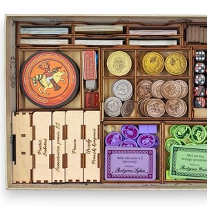 May include: Wooden board game organizer with compartments for cards, dice, tokens, and coins. Includes a circular game piece with a knight on horseback and various game components in a wooden box.