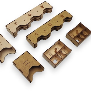May include: A collection of laser-cut wooden game organizers. The set includes several rectangular trays, some with divided compartments, and two card holders. The organizers are light brown with engraved details and text.