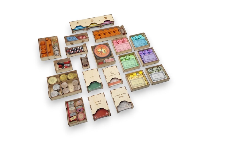 May include: A collection of wooden game organizers, featuring various compartments and boxes. The organizers hold game pieces like dice, tokens, and cards. The boxes are in different colors, including orange, green, and pink.