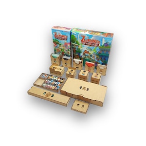 Peut inclure: Un jeu de société avec deux boîtes colorées et plusieurs composants en bois. Les boîtes présentent des illustrations et du texte. Diverses boîtes et plateaux en bois sont disposés autour des boîtes, suggérant des pièces de jeu et du rangement.