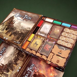 May include: A board game titled Gra o Tron with an open box containing organised game components. The set includes decks of illustrated cards, stacks of circular tokens, and coloured plastic markers arranged in a wooden insert tray.