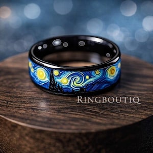 Könnte beinhalten: Ein schwarzer Ring mit einem blau-gelben Sternennacht-Design. Der Ring zeigt eine detaillierte Darstellung von Van Goghs Gemälde "Sternennacht". Der Text "RINGBOUTIQ" ist auf der Holzoberfläche sichtbar.