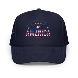 Peut inclure: Casquette de camionneur bleu marine avec un dos en filet et une visière incurvée. L'avant de la casquette présente un aigle avec le texte "UNITED STATES OF AMERICA" et le mot "AMERICA" en rouge, blanc et bleu.