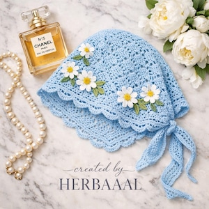 May include: A pale blue crochet bonnet decorated with white daisy appliqués and green leaves. The bonnet features a scalloped edge and ties. A bottle of Chanel perfume, a pearl necklace, and flowers are in the background. Text reads "created by HERBAAAL".