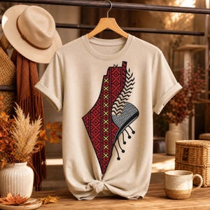 Peut inclure: Un t-shirt beige à manches courtes arborant un grand motif graphique en forme de carte, rempli de motifs géométriques rouges et noirs, de détails en croix jaunes et d'une section à damier noir et blanc avec des accents circulaires pendants.