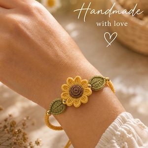 Peut inclure: Un bracelet fait main en crochet jaune avec un tournesol et deux feuilles vertes. Le bracelet comporte des perles dorées et le texte "Handmade with love". Le tournesol a un centre marron.