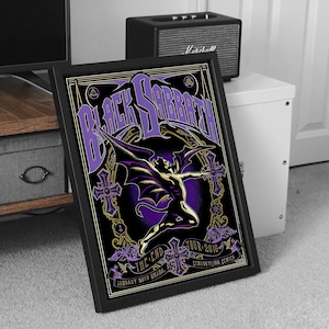 May include: Framed Black Sabbath concert poster. The poster features the band's name in large purple letters, a winged figure, and the tour details. The design is set against a black background with gold accents.