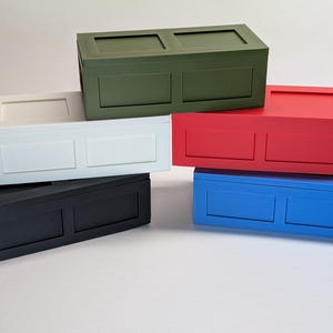 May include: A collection of six rectangular wooden boxes in various colors: green, white, black, red, and blue. Each box has a recessed panel design on the front and a flat top. The boxes are stacked and arranged against a white background.