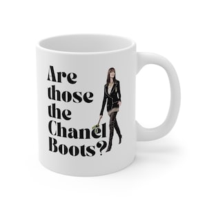 May include: White ceramic mug with the text "Are those the Chanel Boots?" in black. The mug features an illustration of a woman in a black jacket and boots. The mug has a white handle.