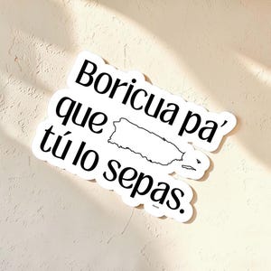 Peut inclure: Un autocollant blanc avec du texte noir qui dit "Borícua pa' que tú lo sepas." Un contour noir de Porto Rico est au centre. L'autocollant est sur une surface beige.