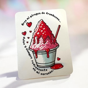 Puede incluir: Una tarjeta blanca con una ilustración de dibujos animados de un postre de hielo raspado de frambuesa en una taza. El hielo raspado está cubierto con jarabe rojo y una pajita roja. La tarjeta tiene texto en español y pequeños corazones rojos.