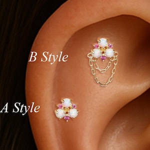 Puede incluir: Se muestran dos piercings dorados para la oreja, etiquetados como "A Style" y "B Style". "A Style" es un pequeño pendiente con piedras blancas, rosas y amarillas. "B Style" tiene un diseño similar, con cadenas colgantes.