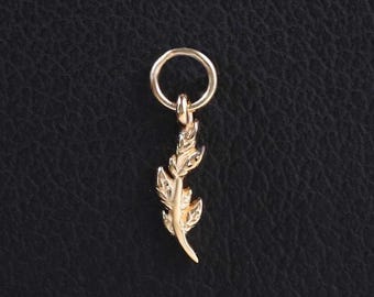May include: A small gold-toned metal charm shaped like a delicate feather, featuring intricate etched details along its surface. The feather charm is attached to a simple, circular gold-toned jump ring, designed for easy attachment to a chain or bracelet.