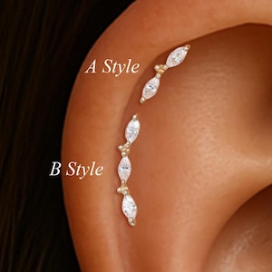 May include: Close-up of an ear with two styles of gold earrings. "A Style" features two small earrings, while "B Style" has a series of three earrings. Each earring has a gold setting with a clear, oval-shaped stone.