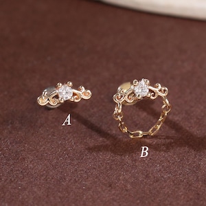 May include: Two pieces of gold jewellery with clear gemstones. One is a stud earring with a curved design, and the other is a ring with a chain-link band. Both pieces have a similar design with a central gemstone.