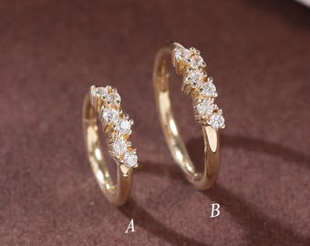 Puede incluir: Dos pendientes de aro dorados, cada uno adornado con una serie de pequeñas y brillantes piedras preciosas blancas. Los pendientes se muestran sobre una superficie marrón, con un objeto blanco curvado en el fondo. Los pendientes están etiquetados A y B.
