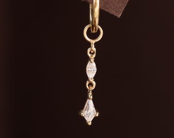 May include: A single gold earring with a dangling design. The earring features a small hoop at the top, connected to a chain with two small, elongated, clear stones and a larger, diamond-shaped clear stone at the bottom. The earring is set against a brown background.
