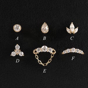 May include: Six pieces of jewellery are arranged on a black surface. The collection includes earrings and a ring, all crafted from gold-coloured metal and adorned with clear gemstones. The gemstones are in diverse shapes, such as round, teardrop, and floral.