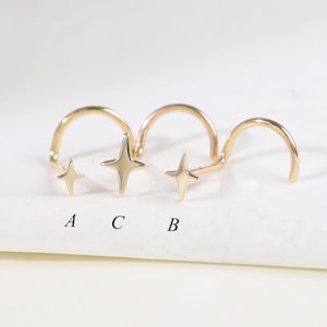 May include: Three gold-colored nose rings with star-shaped charms. Each ring has a different star design. The letters A, C, and B are printed below the rings. The rings are displayed on a white surface.