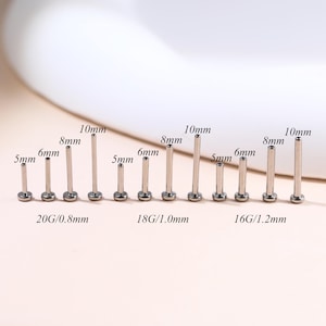 May include: A collection of silver-colored body jewelry studs in varying lengths and gauges. The studs range from 5mm to 10mm in length, with gauges of 20G/0.8mm, 18G/1.0mm, and 16G/1.2mm. The jewelry is displayed against a soft, neutral background.