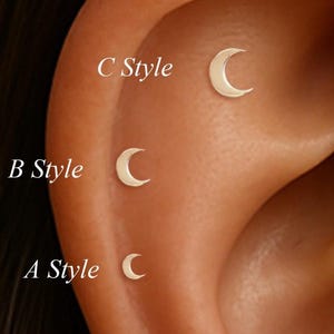 Puede incluir: Primer plano de una oreja con tres pendientes pequeños en forma de media luna. Los pendientes están etiquetados como Estilo A, Estilo B y Estilo C. Los pendientes son de color claro y metálico.