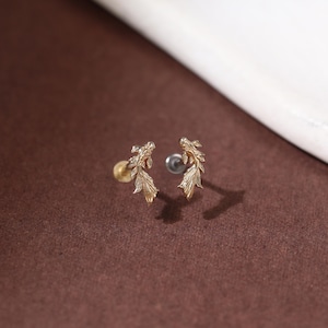 May include: A pair of gold-toned stud earrings shaped like koi fish with detailed scales and flowing fins. Each earring features a post back mechanism, with one showing a gold-colored backing and the other showing a silver-colored backing.