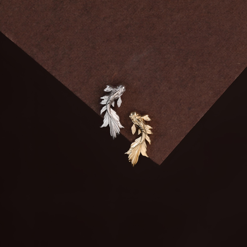 May include: Two fish-shaped pins, one in a polished silver tone and one in a polished gold tone. Each pin features detailed, flowing fins and a slender body, capturing the graceful movement of a swimming fish with a metallic, reflective finish.