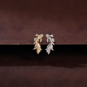May include: A pair of stud earrings shaped like koi fish, with one earring finished in a polished gold tone and the other earring finished in a polished silver tone, featuring detailed fins and scales on the surface of each fish figure.