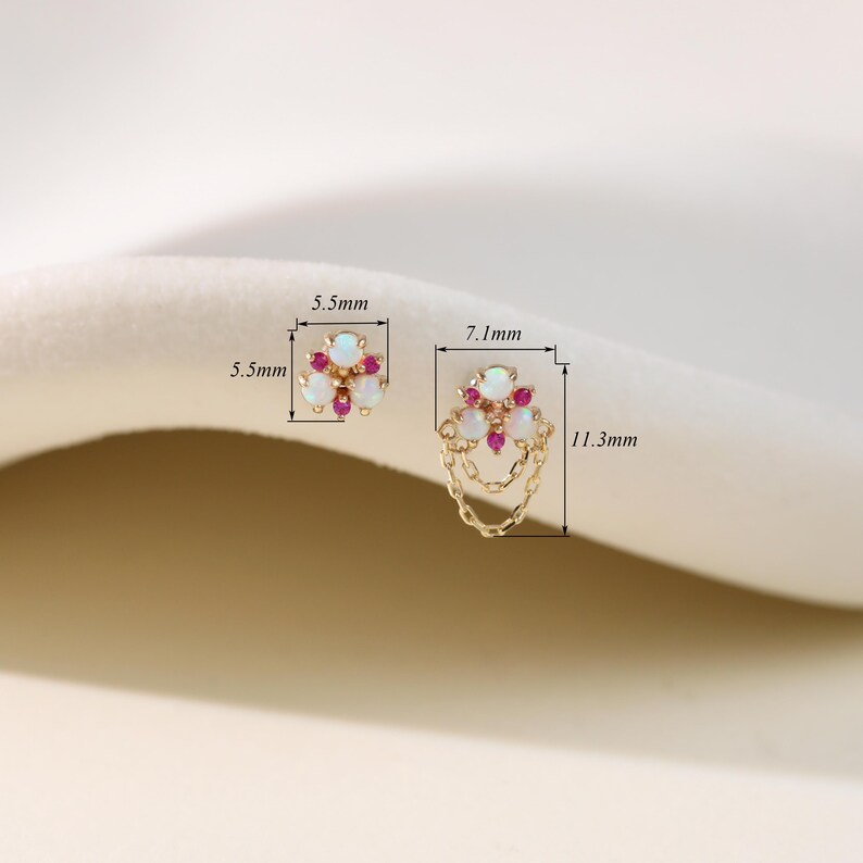 May include: Gold-toned earrings featuring a floral design with white opal and red gemstone accents. One earring measures 5.5mm x 5.5mm, the other 7.1mm x 11.3mm, with a chain detail. The earrings are displayed on a soft, neutral background.