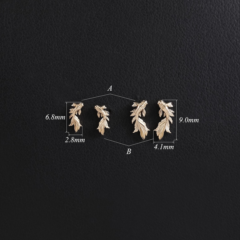 May include: Four gold-toned fish-shaped earrings arranged in two pairs labeled A and B. The smaller pair A measures 6.8mm by 2.8mm, while the larger pair B measures 9.0mm by 4.1mm. Each earring features detailed fins and a textured body design.