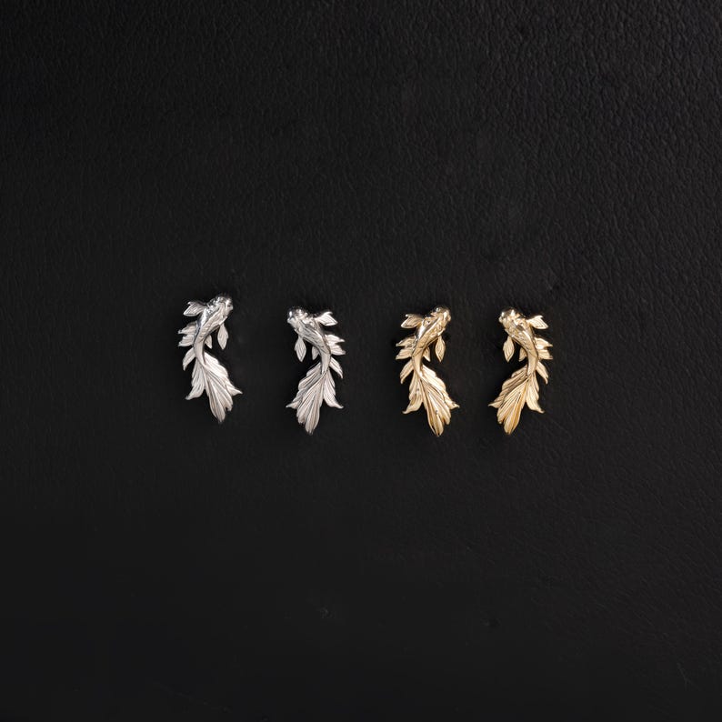 May include: Four stud earrings shaped like koi fish, arranged in a row. The two earrings on the left are silver-toned with detailed fins and scales, while the two earrings on the right are gold-toned with the same intricate fish design.