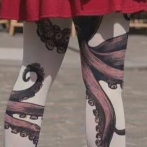 May include: White leggings featuring a detailed graphic print of dark purple and black octopus tentacles with visible suction cups, extending across the legs. The leggings are worn underneath a solid red skirt that sits at the waist.