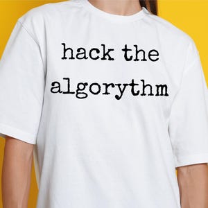 Puede incluir: Camiseta blanca con la frase "hack the algorythm" impresa en negro y en negrita. La camiseta tiene mangas cortas y cuello redondo. El fondo es amarillo liso.
