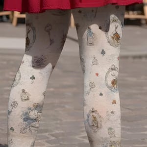 May include: Off-white tights featuring a repeating pattern of vintage-style illustrations, including rabbits in ornate frames, pocket watches, keys, and small card suit symbols like clubs and diamonds, worn under a solid red skirt.
