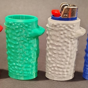 May include: Four 3D printed lighter covers in red, green, gray, and blue. Each cover has a textured, tree bark-like design.