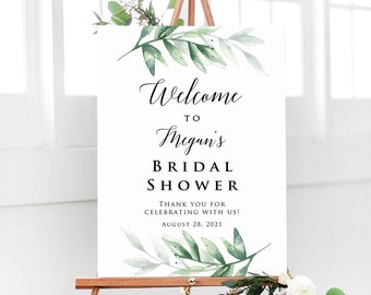 May include: A white sign with green watercolor leaves and the text "Welcome to Megan's Bridal Shower. Thank you for celebrating with us! August 28, 2021."