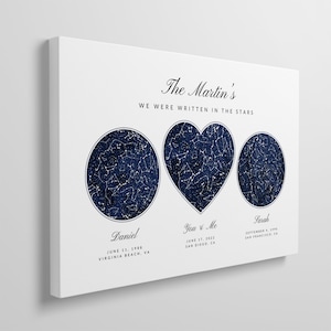 May include: A white canvas print with the text "The Martin's We Were Written In The Stars" at the top. Three star constellations are displayed in the center of the print: a circle, a heart, and another circle. The constellations are in a dark blue color. Below each constellation is text with a name and date. The text reads: "Daniel June 11, 1988 Virginia Beach, VA", "You & Me June 17, 2022 San Diego, CA", and "Sarah September 4, 1998 San Francisco, CA".
