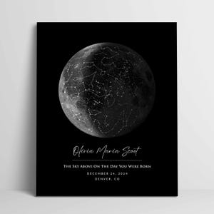 May include: A black rectangular poster featuring a circular moon graphic overlaid with white constellation lines and stars. The text reads: Olivia Maria Scoot, THE SKY ABOVE ON THE DAY YOU WERE BORN, DECEMBER 24, 2024, DENVER, CO in white lettering.
