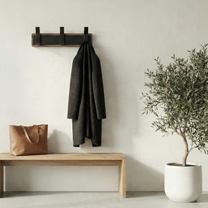 Pu&ograve; includere: Una scena d'ingresso minimalista con una panca in legno, un attaccapanni con un cappotto scuro e una borsa tote in pelle. Un albero di ulivo in vaso aggiunge un tocco di verde. Il muro &egrave; dipinto di un colore neutro.