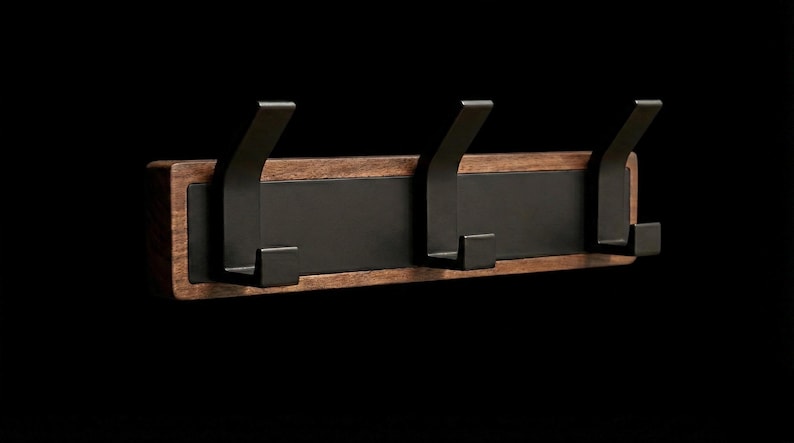 Pu&ograve; includere: Un attaccapanni da parete con tre ganci in metallo nero. I ganci sono montati su una tavola rettangolare in legno con finitura marrone scuro e un pannello centrale nero. Design minimalista e moderno.